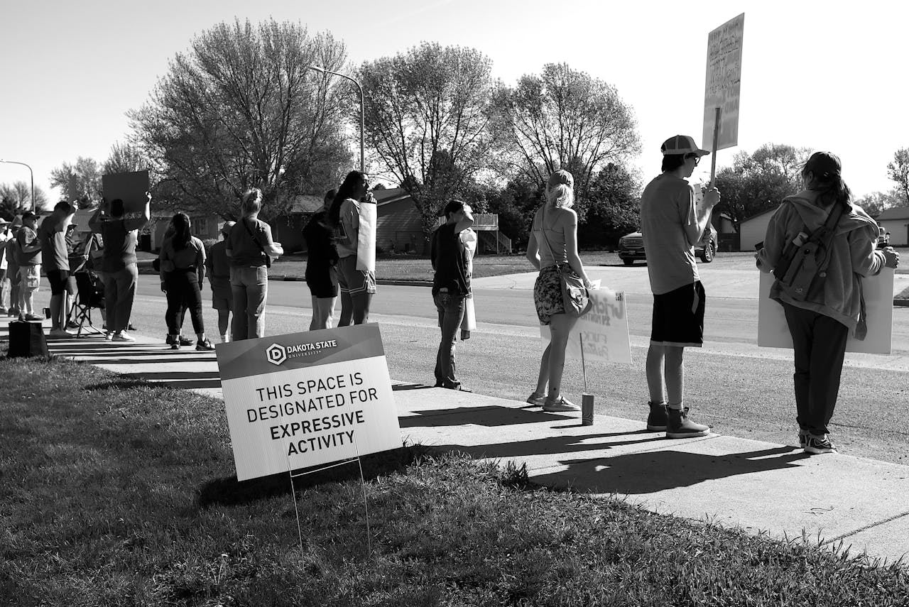 A group of people holding signs in a designated expressive activity zone during a peaceful protest outdoors.